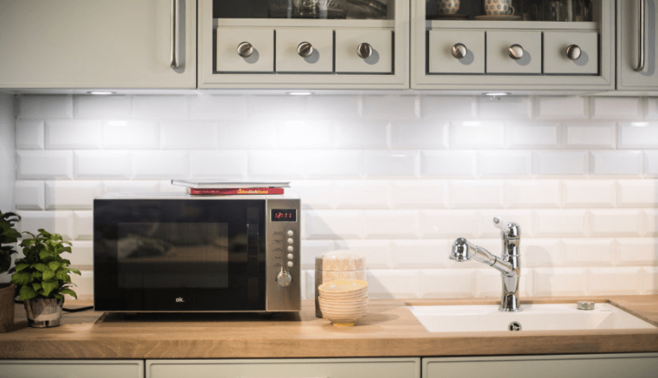 An ok. microwave with crockery, sink and books in a modern kitchen, panorama