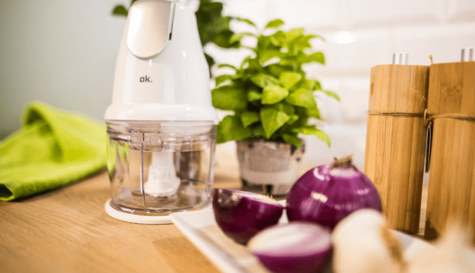 Broyeur de la marque ok., sur un support en bois, à côté d’assiettes avec oignons et ail, salière et poivrier, environnement de cuisine moderne, gros plan