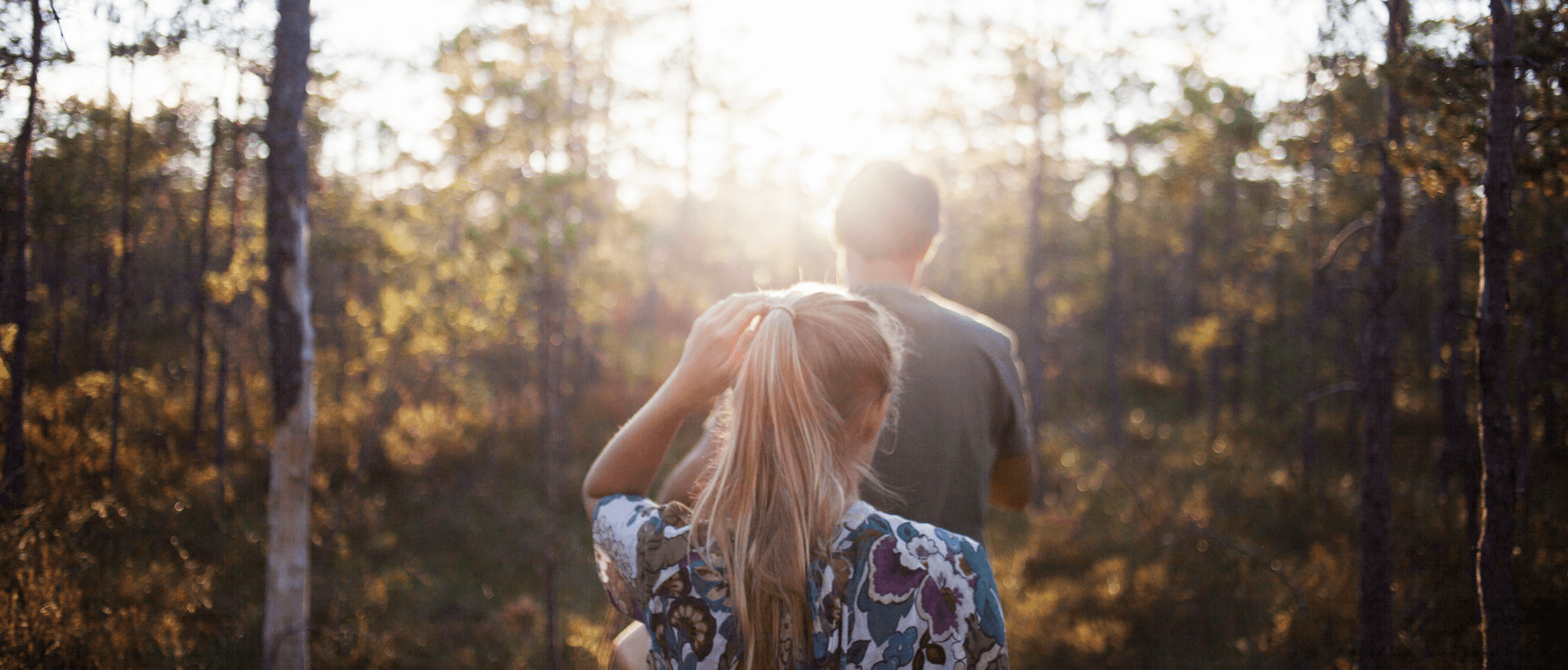 Eine junge Frau folgt einem jungen Mann in den Wald, sommerliche Atmosphäre und Sonneneinfall, Rückansicht